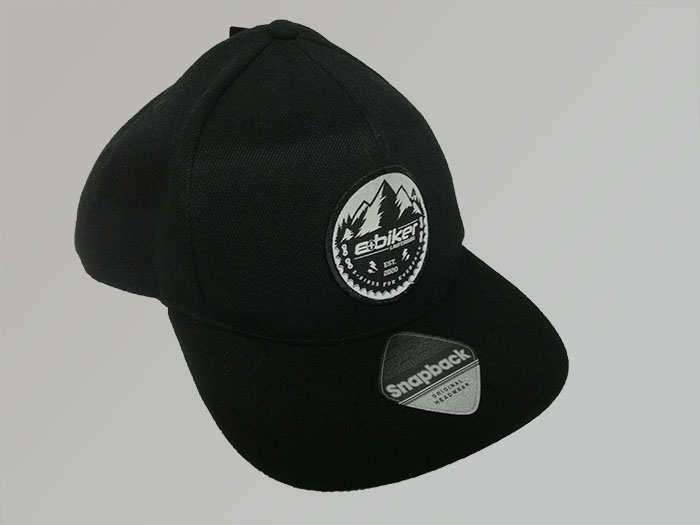 Web-Patch mit dem Motiv "E-Biker" auf einer schwarzen Snapback-Mütze. Textilveredlung von DOWE